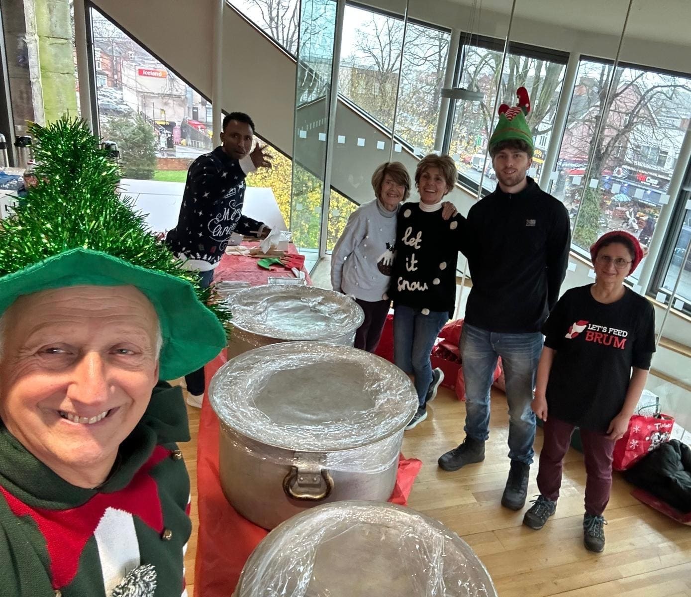 Freiwillige von Let's Feed Brum in Weihnachtspullovern und Elfenmützen, bereit neben den abgedeckten Kochtöpfen
